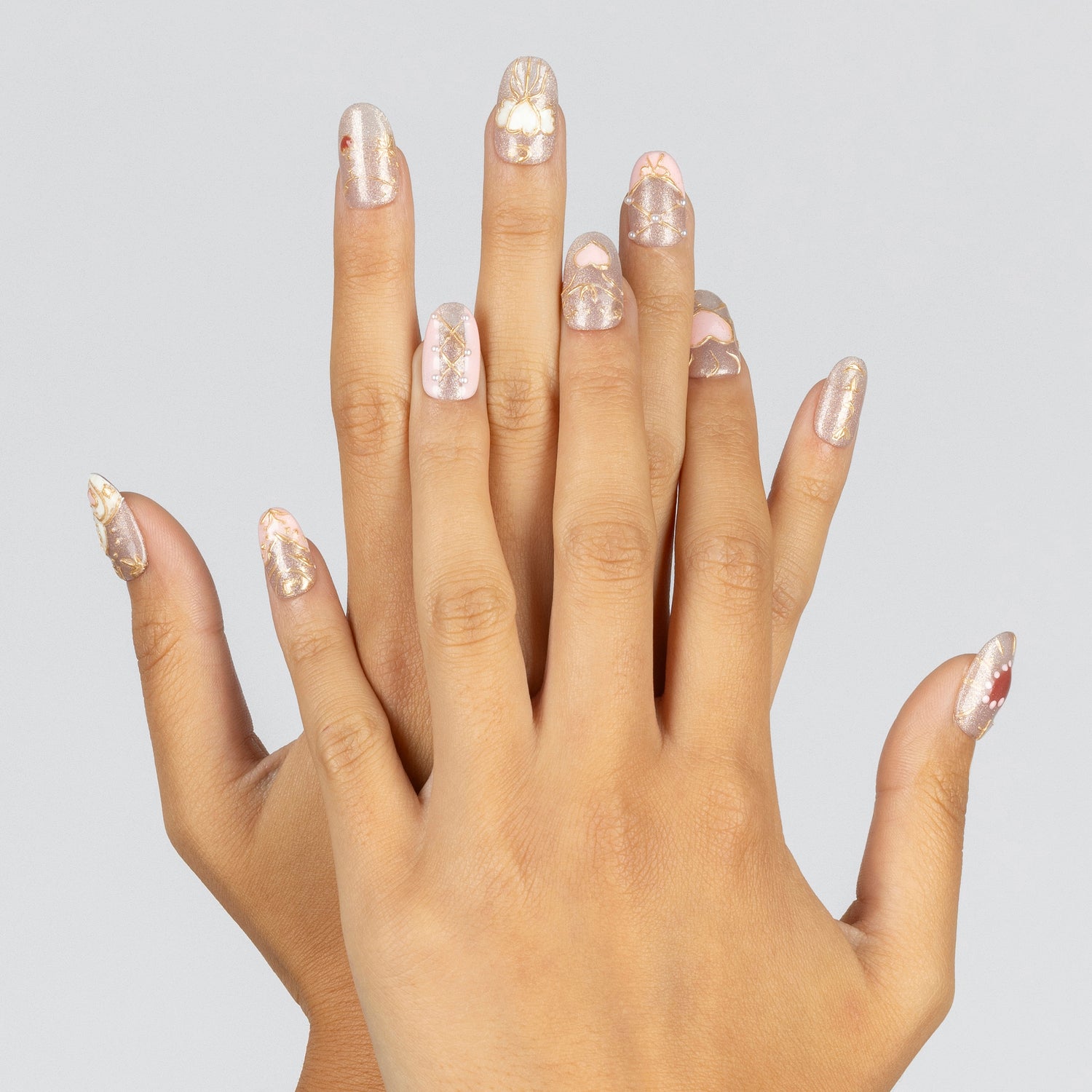 A pair of hands with manicured nails painted in a glossy pale pink and white glitter pattern, set against a solid light gray background.