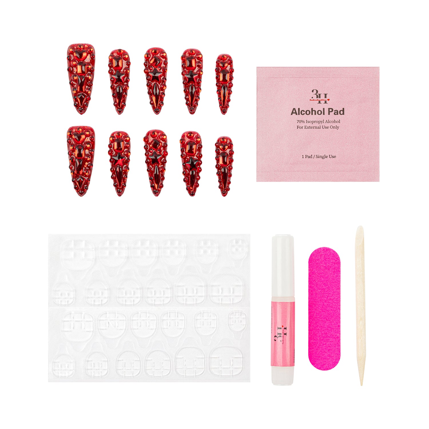 A nail art kit on a white background featuring ten red rhinestone-covered stiletto-shaped press-on nails, a pink packet of alcohol pads, adhesive tabs, a pink nail file, a pink nail polish tube, and a wooden cuticle stick.