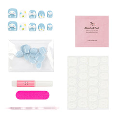 A nail art kit laid out on a white background, including decorative false nails in light blue and white with pastel accents, a pink packet labeled Alcohol Pad, a clear bag of light blue nail tips, a pink-and-white glue tube, a pink nail file, and a sheet of adhesive tabs.