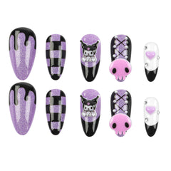 A set of ten Almond-shaped press-on nails arranged in two rows on a plain white background. The nails feature various designs including glittery purple and black dripping, black and purple checkered patterns, a cartoon character design, a pink skull with rhinestones, and a white and black nail with a pink heart accent.