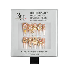A 10-piece press-on nail kit in its original packaging, featuring long coffin-shaped nails with gold glitter, rhinestones, and floral embellishments. The packaging is white with black text and a clear window displaying the nails.