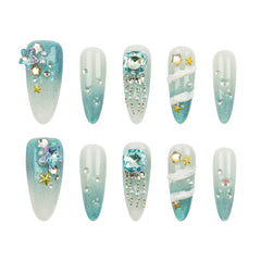 Set of ten artificial press-on nails arranged in two rows of five on a plain white background. The nails feature a light blue to white gradient with various embellishments including rhinestones, pearls, silver beads, and gold star accents.