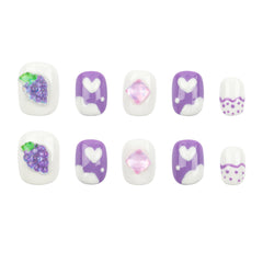 A set of ten press-on nails arranged in two rows of five on a plain white background. The nails feature a white base with purple and white heart designs, one nail with purple glittery grapes with green leaves, one pink glittery diamond, and one white nail with purple wavy lines and small purple dots.