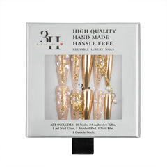 A boxed set of reusable luxury press-on nails in a white retail package. The nails are metallic gold with glitter and pearl embellishments, visible through a clear window on the front of the box.