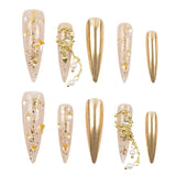 A set of artificial press-on nails arranged on a plain white background. The nails are long stiletto-shaped with a glossy metallic gold finish, some decorated with gold glitter, small white pearls, and gold floral charms.