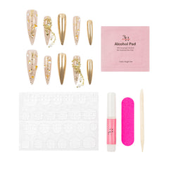 Nail art kit with long coffin-shaped press-on nails in nude and metallic gold with gold foil and chain details, a pink packet of alcohol pad, a white nail stamping plate, a pink nail file, a pink nail polish tube, and a wooden cuticle stick on a white background.