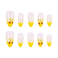 Ten false almond-shaped nails arranged in two rows of five on a plain white background. Each nail has a transparent-to-yellow gradient design with a small yellow bow and two red cherries near the tip.