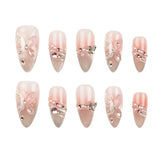 A set of ten false press-on nails arranged in two rows of five on a plain white background. The nails have a glossy pale pink and nude gradient base with decorative designs including 3D pink bows, pearl strands, rhinestones, and butterfly embellishments.
