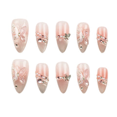 A set of ten false press-on nails arranged in two rows of five on a plain white background. The nails have a glossy pale pink and nude gradient base with decorative designs including 3D pink bows, pearl strands, rhinestones, and butterfly embellishments.