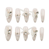 A set of 12 false press-on nails arranged in two rows on a plain white background. The nails feature a glossy nude-pink base with glittery silver tips, embellished with white fabric flowers, clear rhinestones, pearl-like beads, and small butterfly decorations.