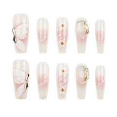 Ten false press-on nails arranged in two rows of five on a plain white background. The nails are clear with fine silver glitter and a soft pink gradient, decorated with white butterfly motifs, small gold flower accents, and metallic ring details.