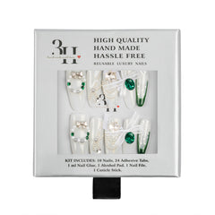 A boxed set of decorative reusable press-on nails in a white package with a clear window showing the nails. The nails are primarily white with green jewel accents, pearl details, and some sheer white ribbon bows.