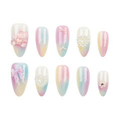Ten-piece press-on nail set with pastel gradient designs in pink, blue, and yellow, featuring various decorative embellishments like bows, pearls, and a teddy bear on a white background.