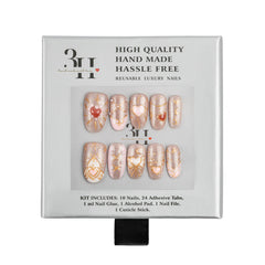 A 10-piece reusable press-on nail kit in its original packaging, featuring metallic rose gold and beige nails with gold glitter patterns and red heart details. 