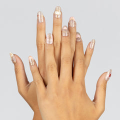 A pair of hands with manicured nails painted in a glossy pale pink and white glitter pattern, set against a solid light gray background.