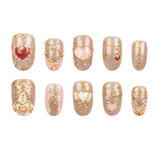Ten decorative press-on nails arranged in two rows on a plain white background. The nails feature a glittery champagne-gold base with gold filigree patterns, pink and white heart motifs, and small pearl-like accents.