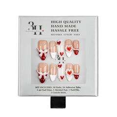 A 3H brand press-on nail kit in its original packaging, featuring 10 nude/beige nails decorated with white bows and pearls, 5 white nails with red hearts, and 5 red nails with white hearts and pearls. 