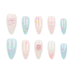 Ten artificial press-on nails arranged in two rows on a plain white background. The nails feature pastel designs including light blue, pale pink, and glossy white, decorated with bows, lace details, flowers, and small green stems.