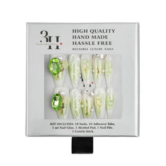 A boxed set of reusable press-on nails in a white package with a clear window showing the nails. The nails are mostly pale green and white with some gold glitter and one bright green gem accent.
