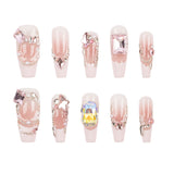 A set of ten coffin-shaped press-on nails with a glossy pale pink base, decorated with various rhinestones, crystals, and metallic gold chain details, arranged in two rows of five on a plain white background.