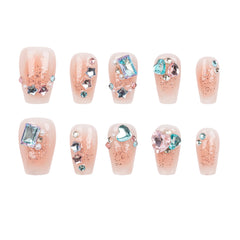 Ten-piece set of false press-on nails with a glossy nude-pink base, glittery rose-gold shimmer, and various pastel rhinestones and gem accents, arranged in two rows of five on a plain white background.