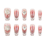 Ten artificial press-on nails arranged in two rows of five on a plain white background. The nails have a sheer pink-to-clear gradient base with silver glitter, some decorated with silver rhinestone leaf motifs, heart charms, and floral embellishments.