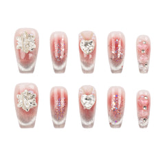 Ten artificial press-on nails arranged in two rows of five on a plain white background. The nails have a sheer pink-to-clear gradient base with silver glitter, some decorated with silver rhinestone leaf motifs, heart charms, and floral embellishments.