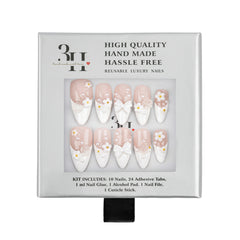 A boxed set of reusable press-on nails on a white background. The package shows ten almond-shaped nails with a pale blush pink base, white French tips, small white daisy motifs, and white bow designs.