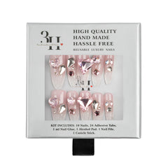 A boxed set of reusable press-on nails in a light gray package. The nails are pale pink with clear rhinestone embellishments and a large heart-shaped pink gem on the front.