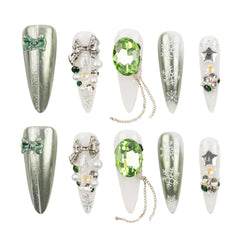 Eight artificial nail tips arranged in two rows on a white background, decorated with silver glitter, white snowflakes, bows, pearls, green gems, and star-shaped rhinestones.