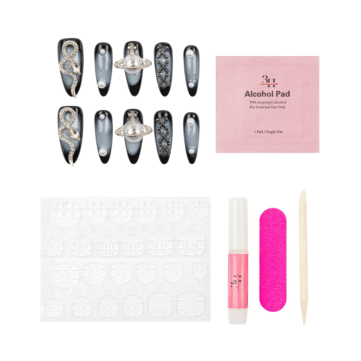 A nail art kit laid out on a white background, including a set of decorative false nails with black, gray, and silver designs, a pink packet labeled 'Alcohol Pad', a white nail stamping plate, a pink nail file, a pink nail polish tube, and a wooden spatula.