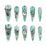 A set of ten long coffin-shaped press-on nails arranged in two rows of five on a plain white background. Each nail features a light teal and white marbled base with silver metallic gothic designs, including winged figures, a snake wrapped in a crown, an eye motif, and chain details.