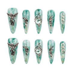 A set of ten long coffin-shaped press-on nails arranged in two rows of five on a plain white background. Each nail features a light teal and white marbled base with silver metallic gothic designs, including winged figures, a snake wrapped in a crown, an eye motif, and chain details.