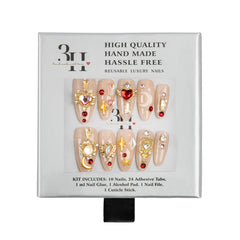 A 10-piece reusable press-on nail kit in its original packaging, featuring beige almond-shaped nails decorated with gold glitter, rhinestones, and red heart accents.