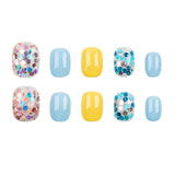 Ten press-on nails arranged in two rows on a white background, featuring light blue, yellow, and glittery multicolor designs.