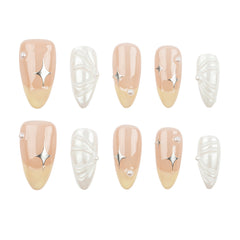 Ten press-on nails arranged in two rows on a plain white background. The nails feature a glossy nude-peach to pale yellow gradient with silver metallic starburst accents and pearl-like bead details, alongside white textured and pearl designs.