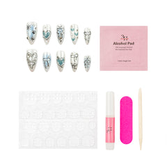 Nail art kit with decorative nail tips, a pink alcohol pad packet, adhesive tabs, a pink nail file, a pink nail polish tube, and a wooden cuticle stick on a white background.