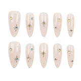 Ten almond-shaped press-on nails arranged in two rows of five on a plain white background. Each nail has a glossy pale blush pink base with small scattered rhinestones and a few starburst accents in gold, silver, blue, and pink.