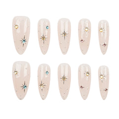 Ten almond-shaped press-on nails arranged in two rows of five on a plain white background. Each nail has a glossy pale blush pink base with small scattered rhinestones and a few starburst accents in gold, silver, blue, and pink.