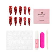 A nail art kit on a white background featuring ten red rhinestone-covered stiletto-shaped press-on nails, a pink packet of alcohol pads, adhesive tabs, a pink nail file, a pink nail polish tube, and a wooden cuticle stick.