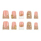 Ten false press-on nails arranged in two rows on a plain white background. The nails feature a glossy light pink top half, a white bottom half on three nails, and ornate gold embellishments including rhinestones, dollar sign charms, and bow details.