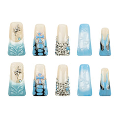 Ten long duck-shaped press-on nails arranged in two rows of five on a plain white background. The nails feature a cream base with light blue gradient designs, silver rhinestone embellishments, and metallic silver cross motifs.