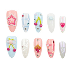 Ten decorative false press-on nails arranged in two rows on a plain white background. The nails feature pastel colors including pink, light blue, white, and iridescent tones, with embellishments such as stars, cherries, bows, hearts, and rhinestones.