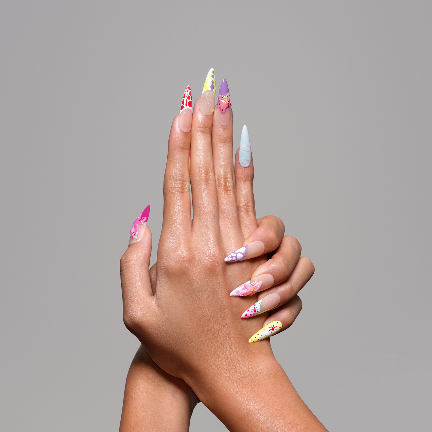 A pair of hands with long, stiletto-shaped nails decorated with colorful floral and geometric patterns, posed against a solid gray background.