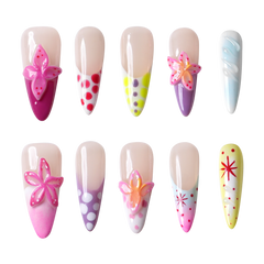 Ten false press-on nails arranged in two rows on a plain white background. The nails have a glossy nude base and various colorful decorative designs including pink flowers, polka dots, stripes, and starburst patterns.