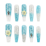 A set of ten long coffin-shaped press-on nails arranged in two rows on a plain white background. The nails feature a light blue and white gradient design with swirl patterns, clear bubble details, and two white flowers with yellow centers and rhinestone accents.