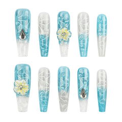 A set of ten long coffin-shaped press-on nails arranged in two rows on a plain white background. The nails feature a light blue and white gradient design with swirl patterns, clear bubble details, and two white flowers with yellow centers and rhinestone accents.
