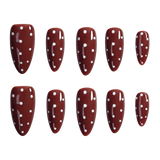 Ten almond-shaped press-on nails with a glossy dark red/burgundy base and white polka dots, arranged in two rows of five on a plain white background.