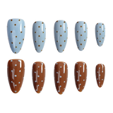 Ten artificial press-on nails arranged in two rows of five on a plain white background. The top row features almond-shaped nails with a light blue base and small gold polka dots.