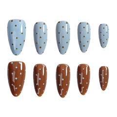 Ten artificial press-on nails arranged in two rows of five on a plain white background. The top row features almond-shaped nails with a light blue base and small gold polka dots.